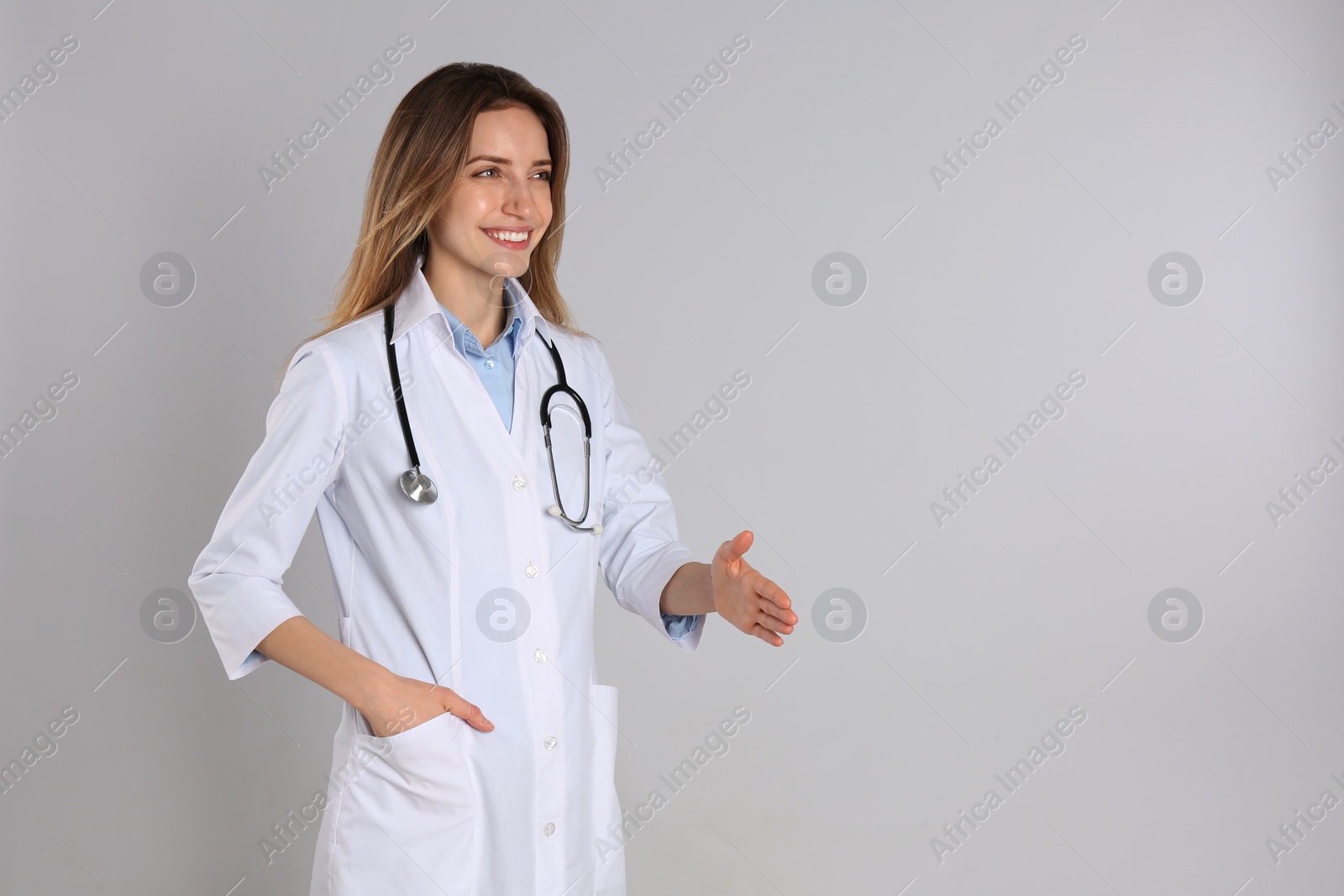 Photo of Happy female doctor offering handshake on light grey background. Space for text