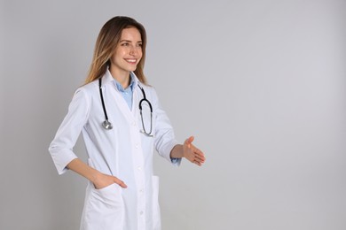 Photo of Happy female doctor offering handshake on light grey background. Space for text