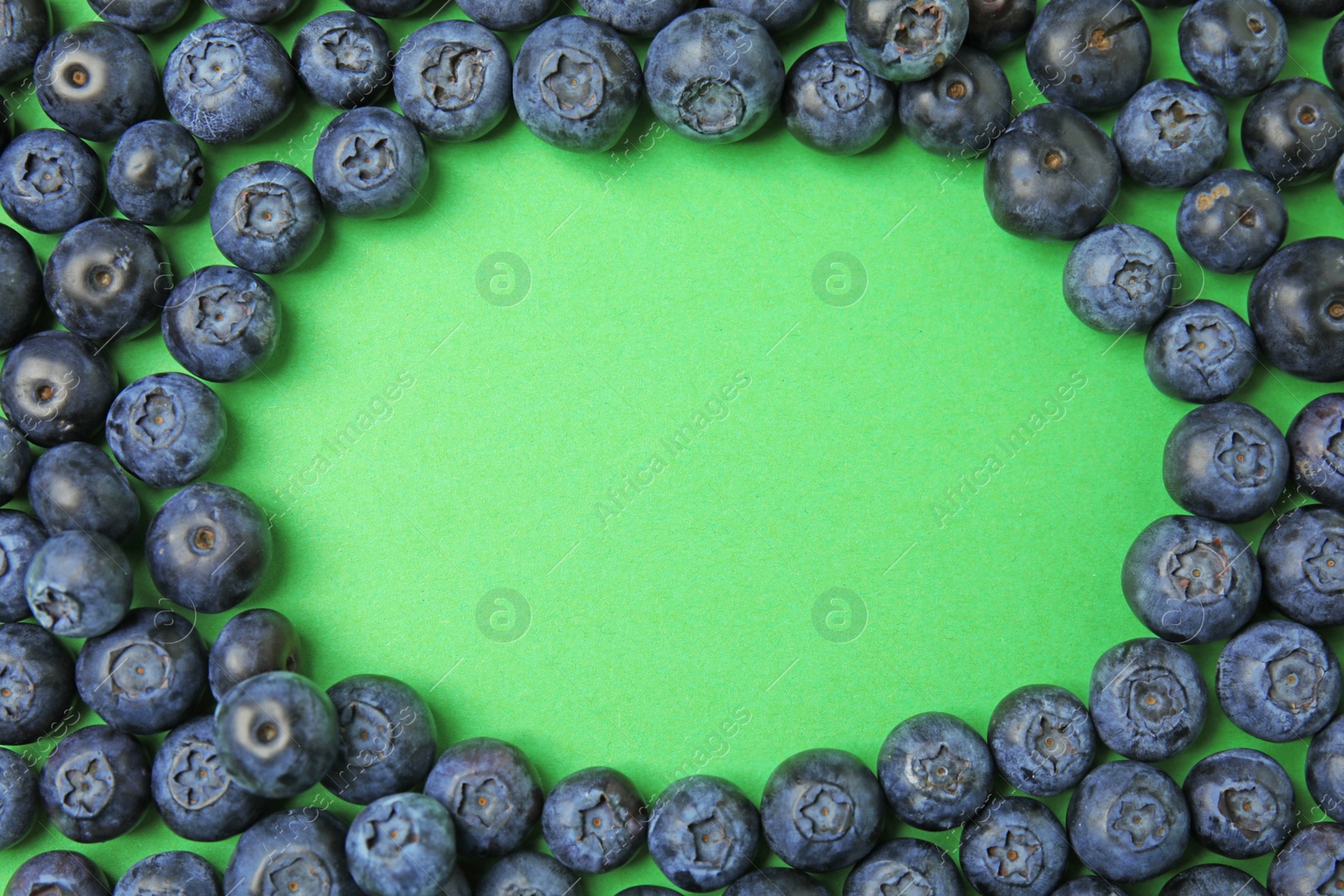 Photo of Frame of ripe blueberries on green background, flat lay with space for text