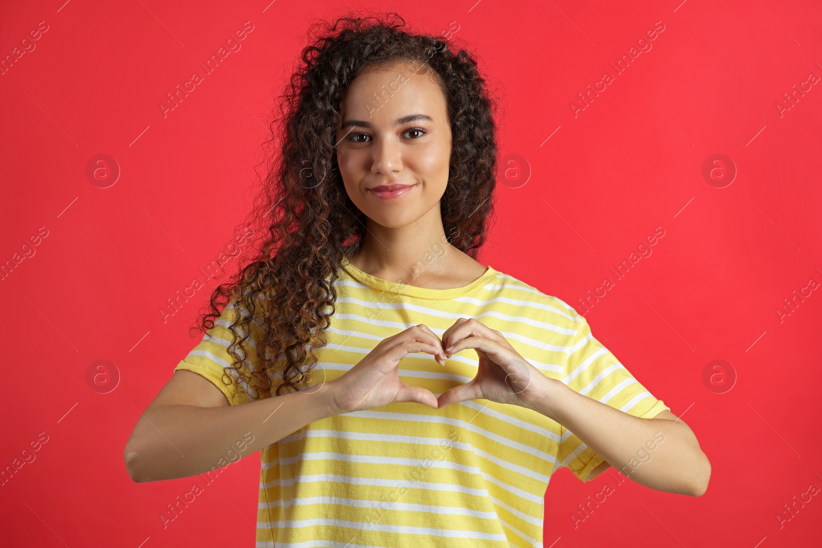 Photo of Happy young African-American woman making heart with hands on red background