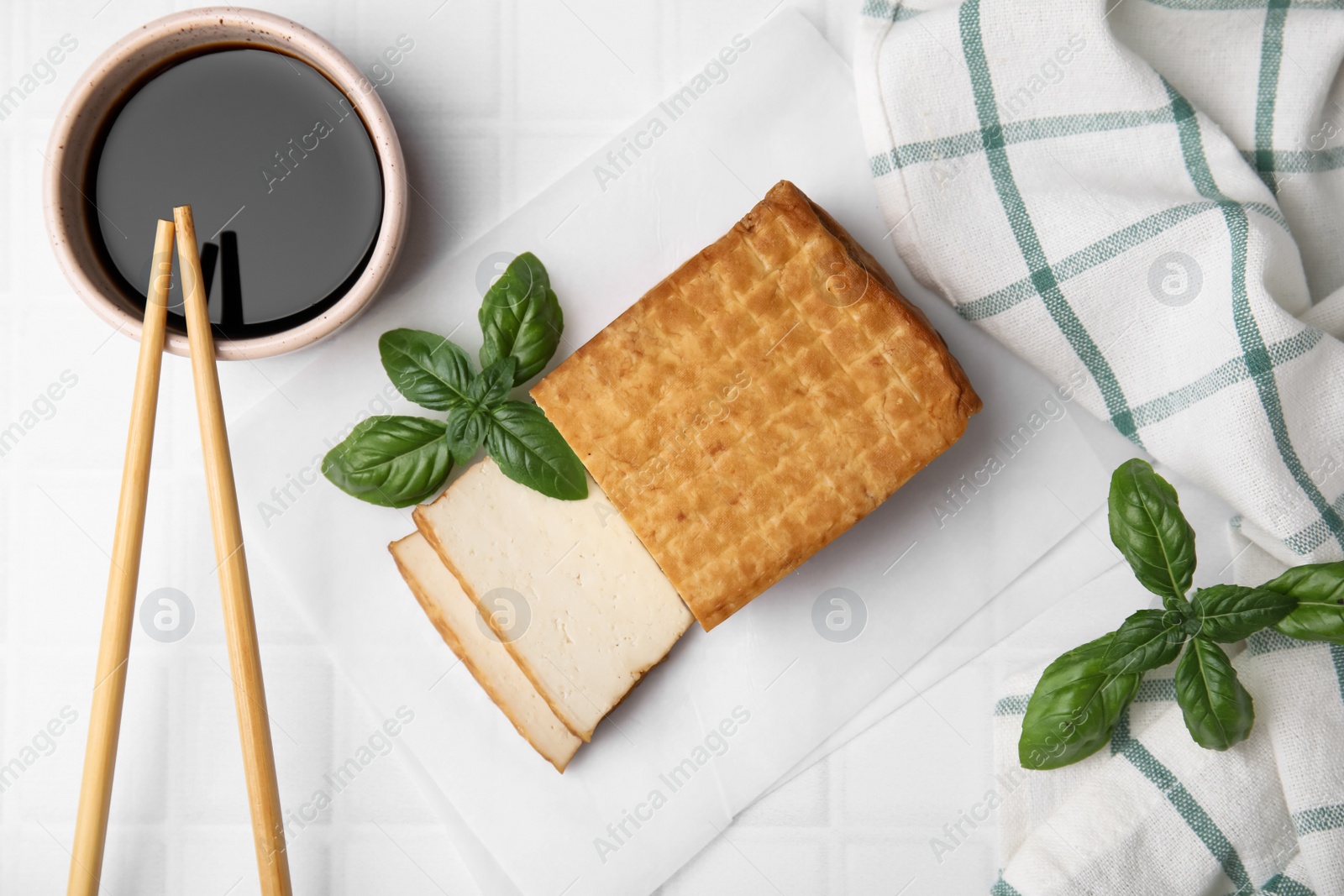 Photo of Delicious smoked tofu, soy sauce and basil on tiled table, flat lay