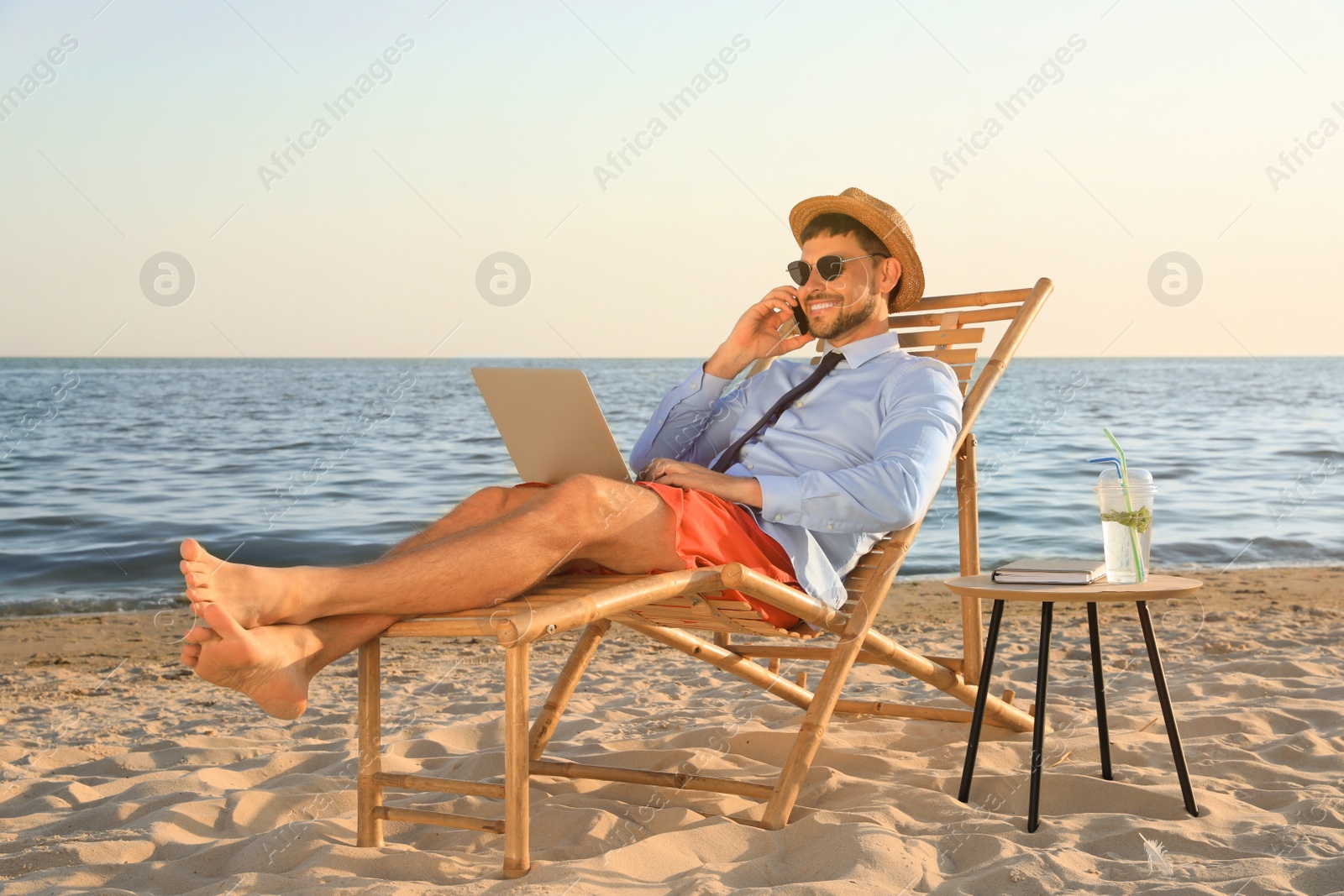 Photo of Man with laptop talking by mobile phone on beach. Business trip