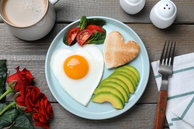 Photo of Romantic breakfast with fried heart shaped egg, avocado and toast on wooden table, flat lay. Valentine's day celebration
