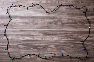 Photo of Frame of Christmas lights on wooden table, top view. Space for text