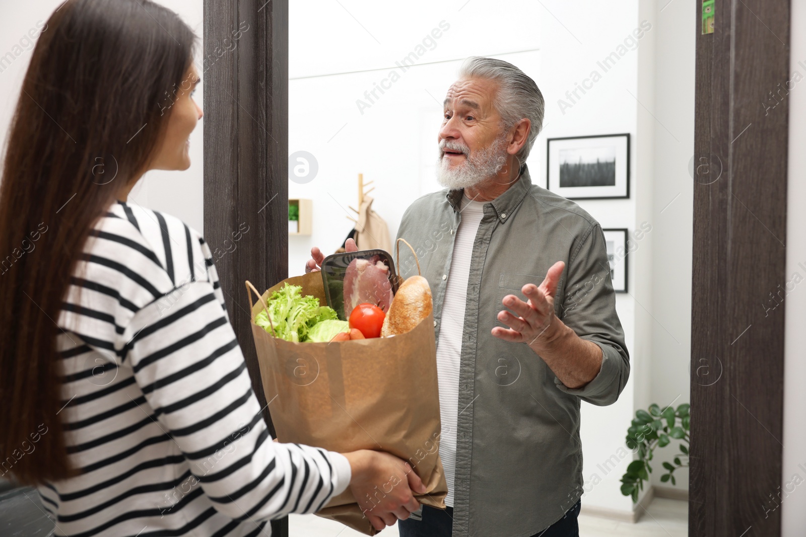 Photo of Courier giving paper bag with food products to senior man indoors