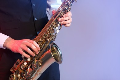Photo of Man in elegant outfit playing saxophone on color background, closeup. Space for text