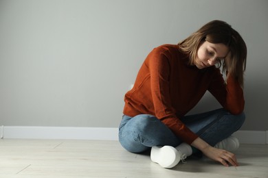 Photo of Sad young woman sitting on floor near grey wall indoors, space for text