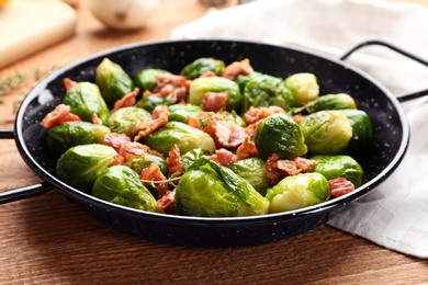 Photo of Tasty roasted Brussels sprouts with bacon on wooden table, closeup