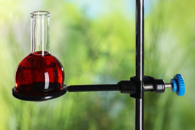 Retort stand and laboratory flask with liquid on blurred background, closeup