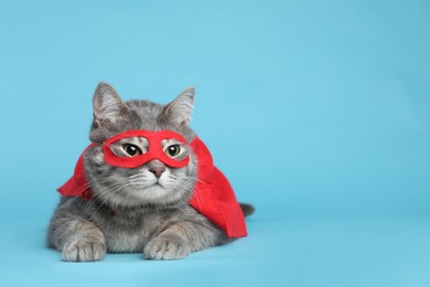 Adorable cat in red superhero cape and mask on light blue background, space for text