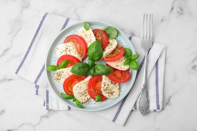 Photo of Caprese salad with tomatoes, mozzarella, basil and spices served on white marble table, top view