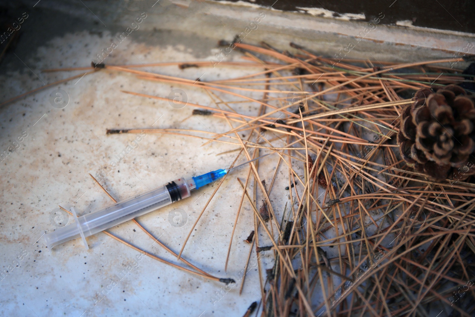 Photo of Disposable syringe with needle and heap of dry branches outdoors