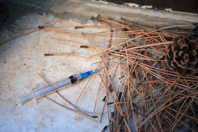 Photo of Disposable syringe with needle and heap of dry branches outdoors