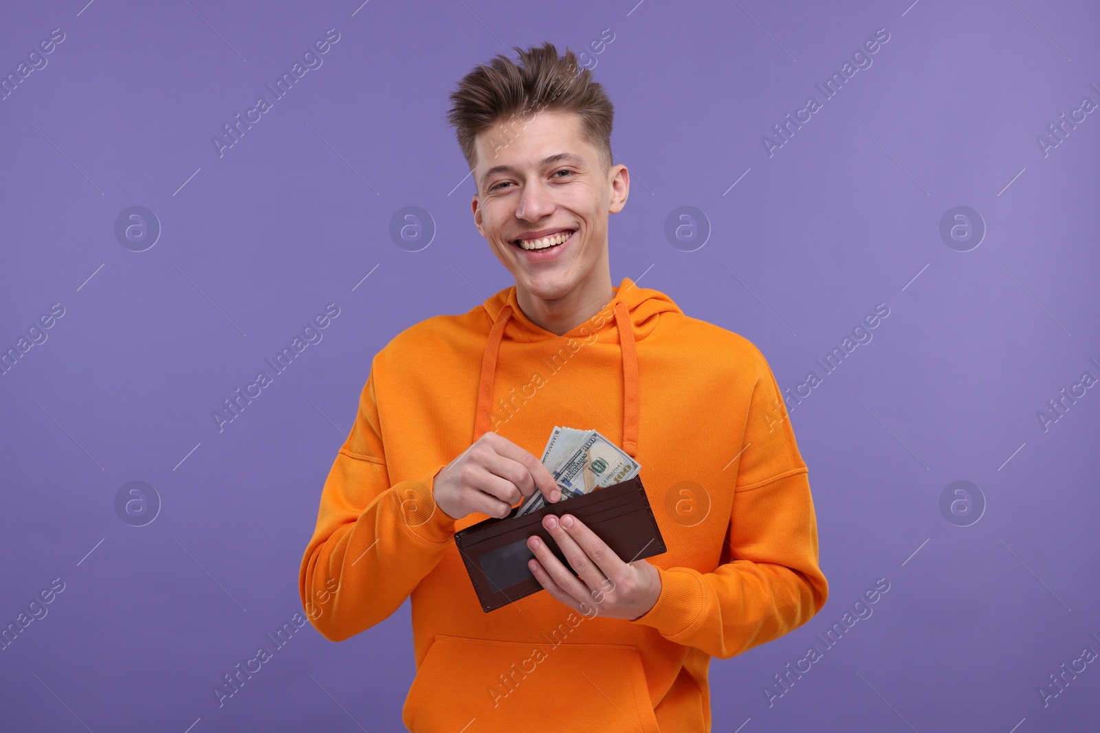 Photo of Happy man putting money into wallet on purple background