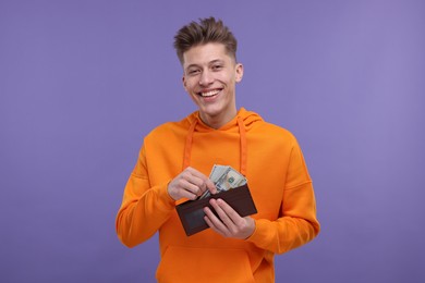 Happy man putting money into wallet on purple background