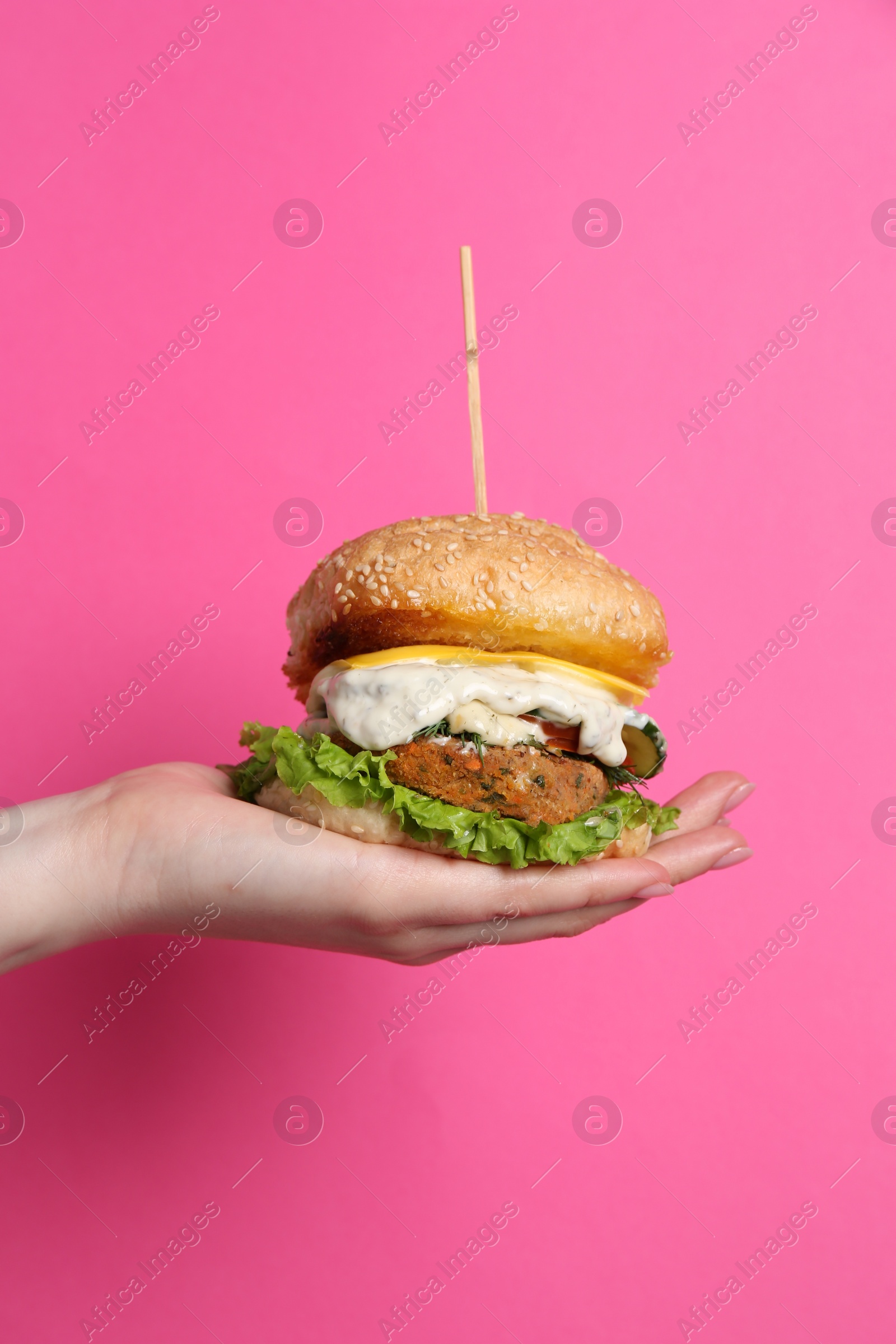 Photo of Woman holding delicious vegetarian burger on pink background, closeup