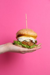 Woman holding delicious vegetarian burger on pink background, closeup