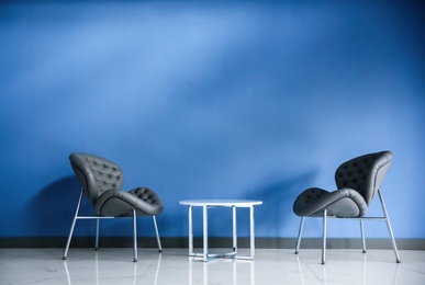 Comfortable armchairs and metal table near blue wall. Modern room interior