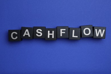 Image of Black wooden cubes with phrase Cash FLow on blue background, flat lay