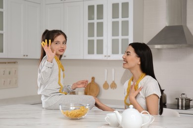 Young mother and her daughter with necklaces made of pasta having fun in kitchen