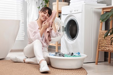 Happy young housewife with laundry near washing machine at home