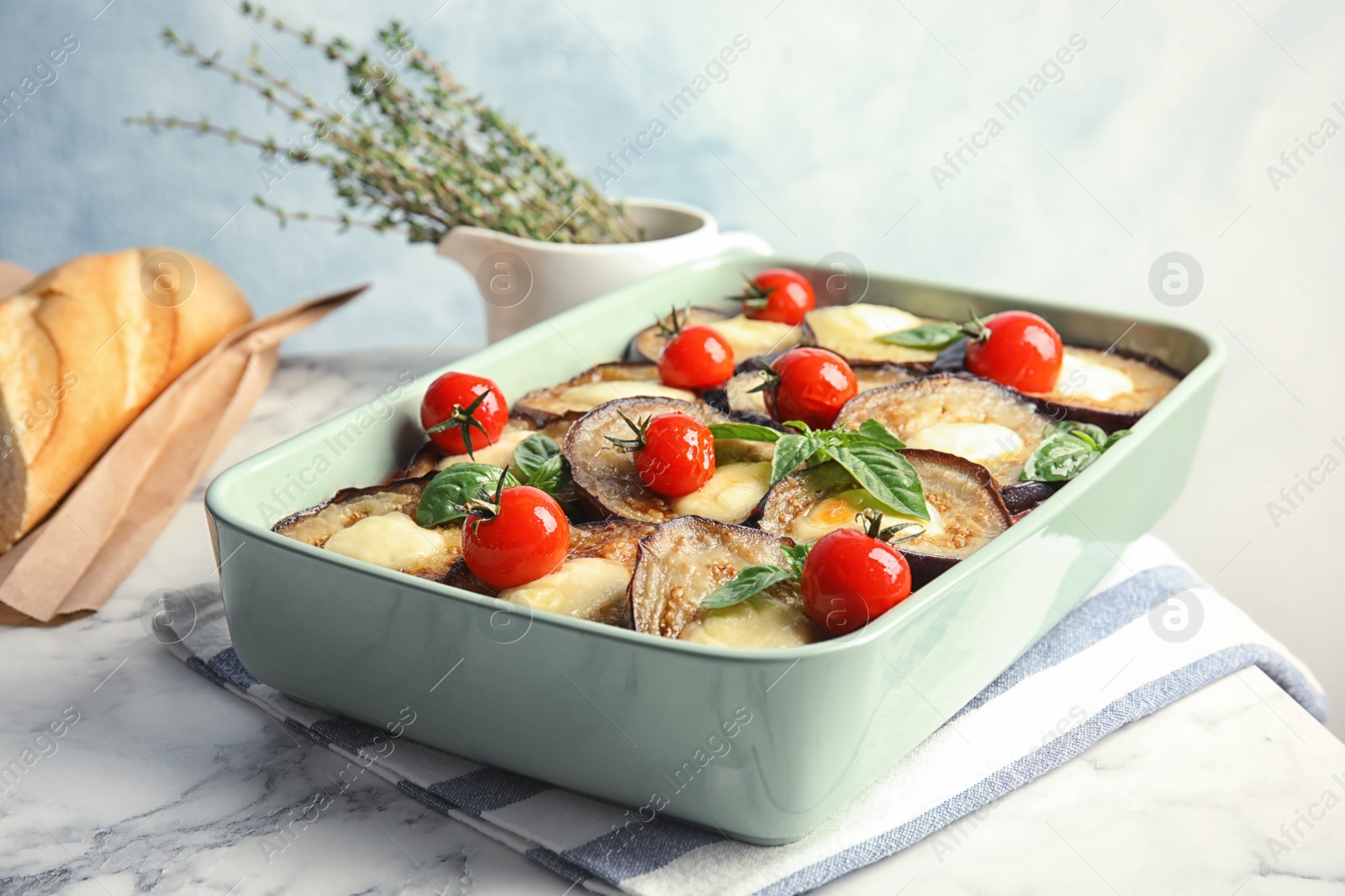 Photo of Baked eggplant with tomatoes, cheese and basil in dishware on marble table