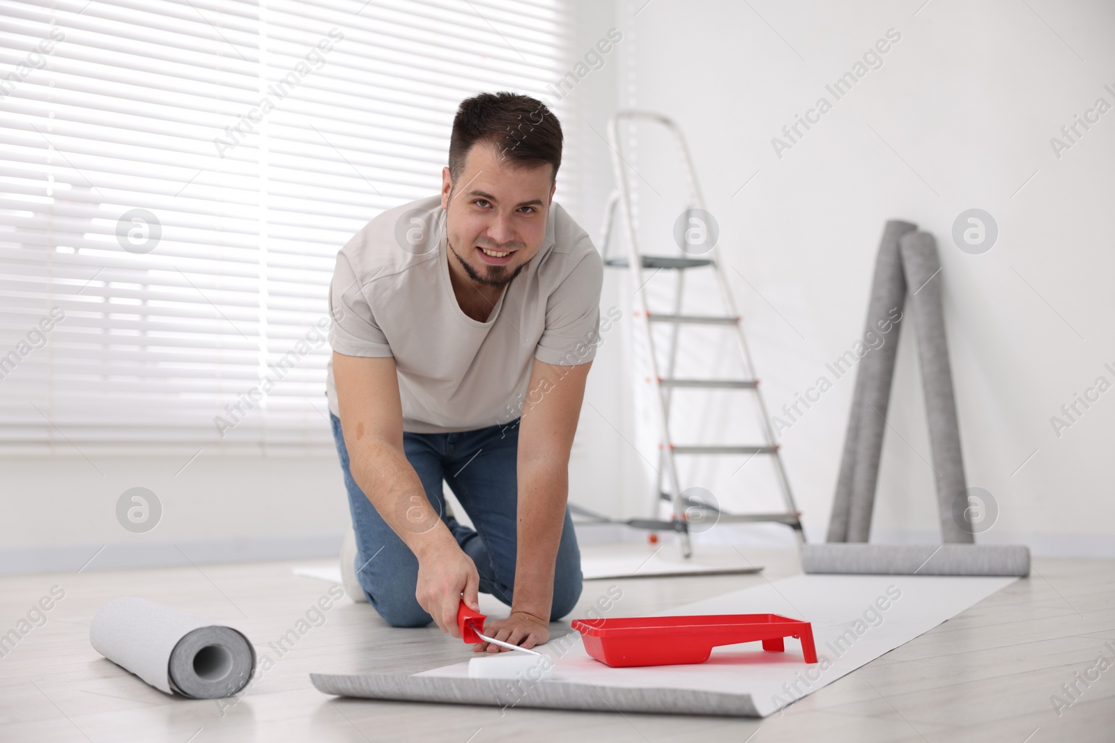 Photo of Man applying glue onto wallpaper sheet in room