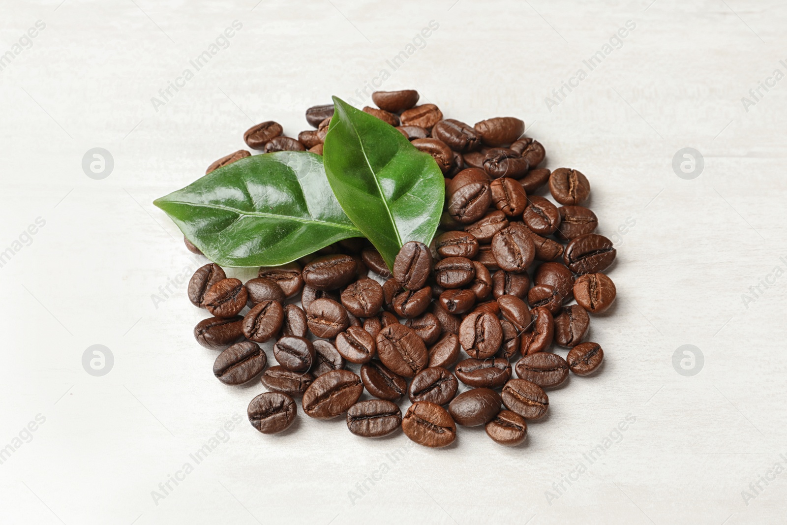 Photo of Roasted coffee beans and green leaves on white background