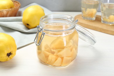 Photo of Delicious quince drink in glass jar and fresh fruits on white wooden table