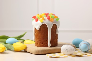 Delicious Easter cake with pieces of candied fruits, painted eggs and tulips on white table indoors