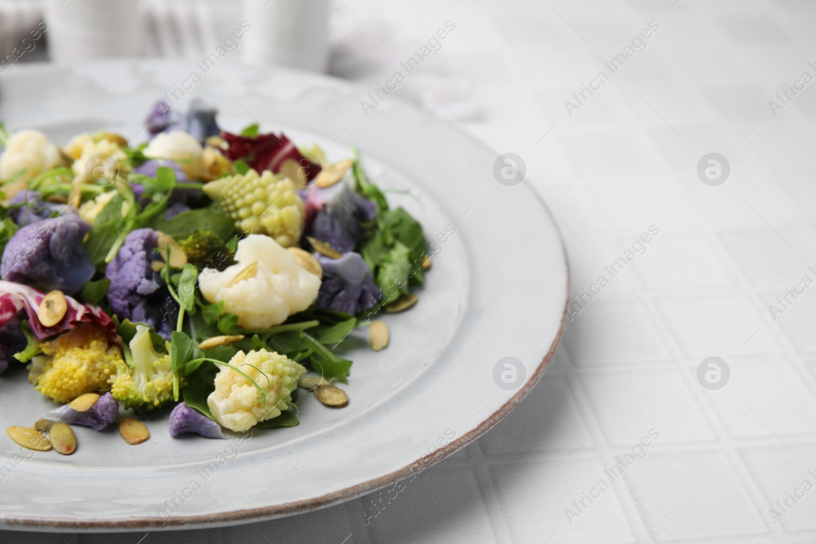 Photo of Delicious salad with cauliflower and pumpkin seeds on white tiled table, closeup. Space for text