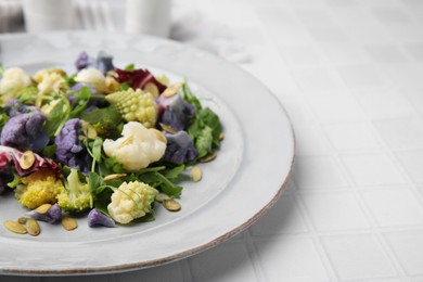 Photo of Delicious salad with cauliflower and pumpkin seeds on white tiled table, closeup. Space for text