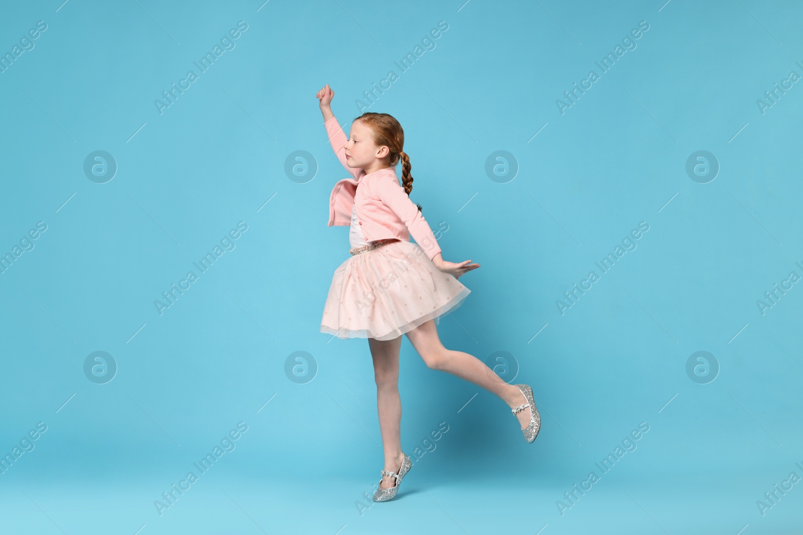 Photo of Cute little girl dancing on light blue background