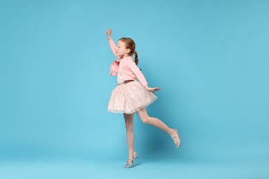 Cute little girl dancing on light blue background