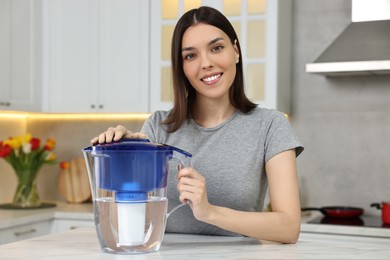 Photo of Woman with filter jug of water in kitchen