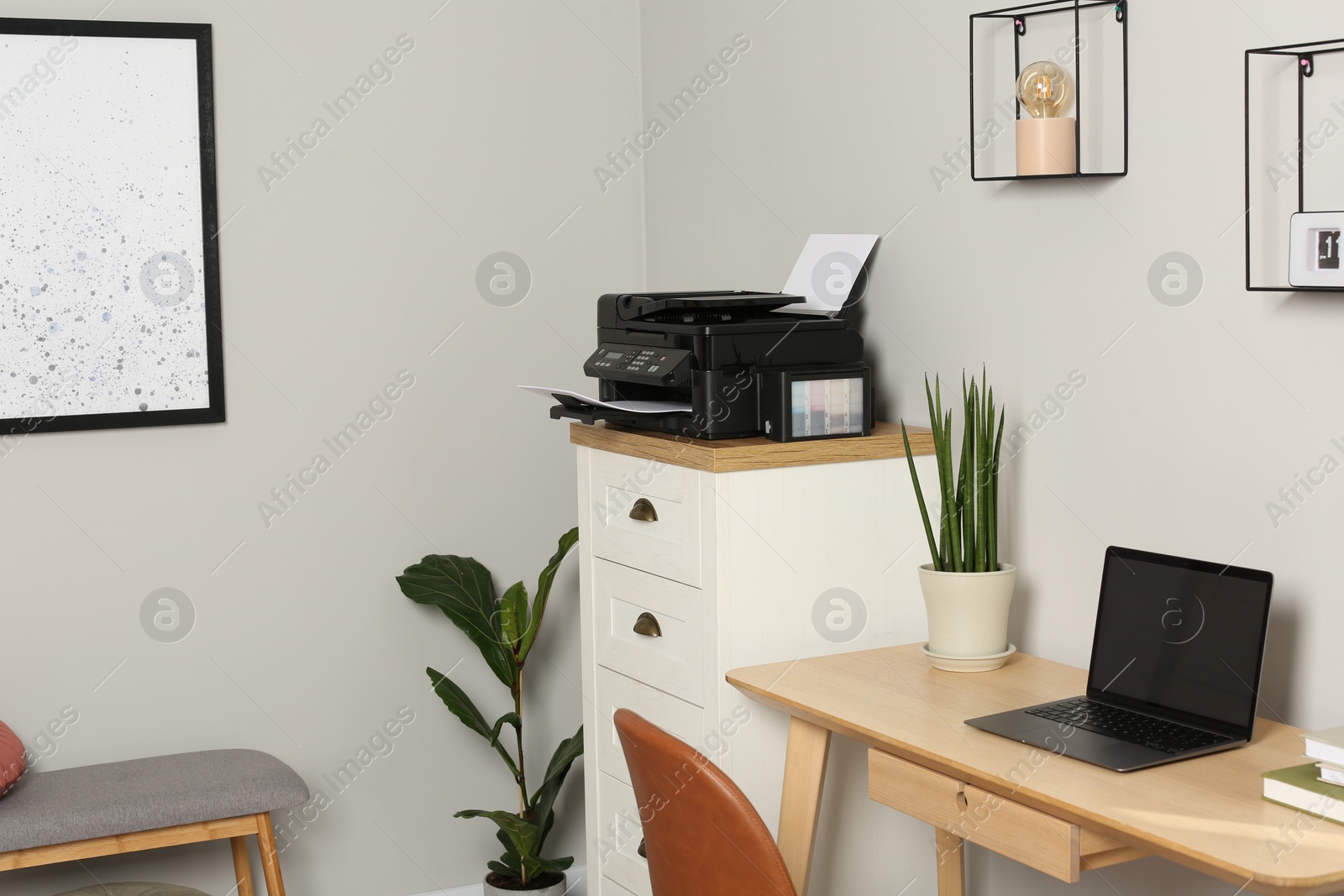 Photo of Modern printer with paper on chest of drawers near wooden table indoors