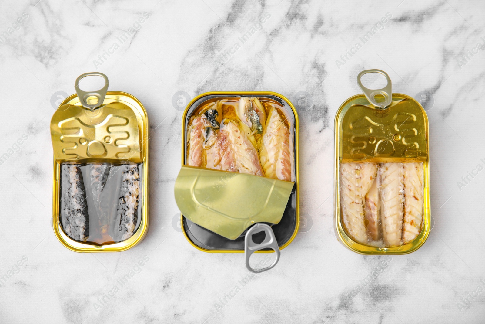 Photo of Open tin cans with mackerel fillets on white marble table, flat lay