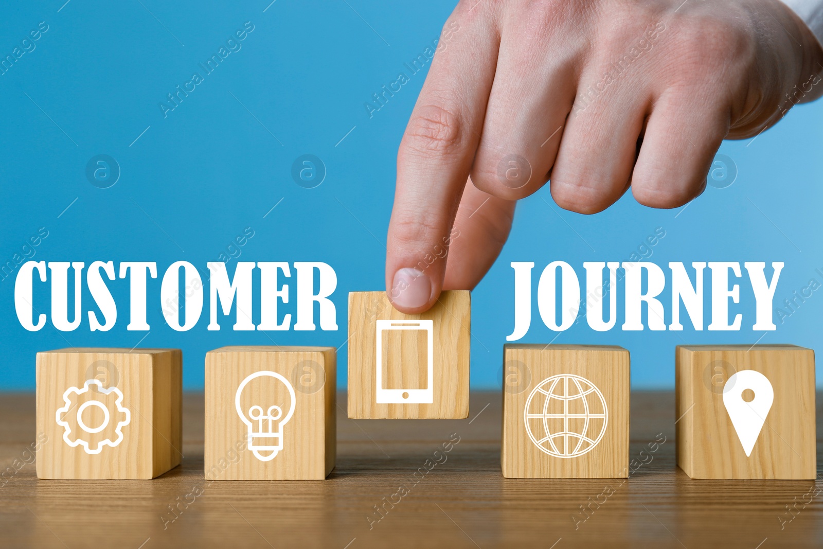 Image of Man arranging cubes with different images in row on wooden table against light blue background, closeup. Customer journey concept