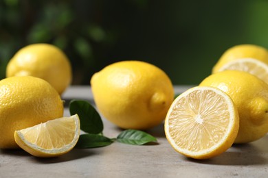 Fresh lemons and green leaves on grey table outdoors, closeup