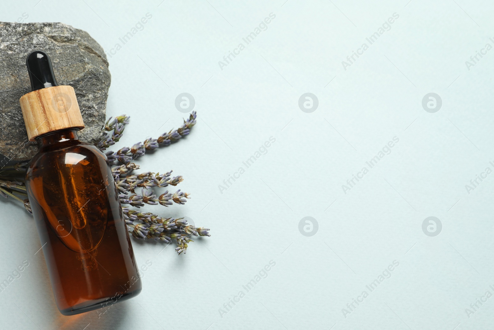 Photo of Flat lay composition with bottle of face serum, stone and beautiful flowers on light grey background. Space for text