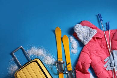Photo of Suitcase with warm clothes and skis on light blue background, flat lay. Winter vacation