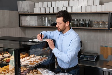 Photo of Handsome business owner with clipboard and pen in bakery shop