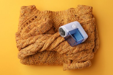 Modern fabric shaver and knitted sweater on orange background, top view