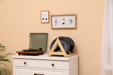 Photo of Vinyl records and player on white wooden drawer dresser near beige wall