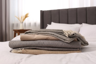 Stack of different folded blankets on bed in room. Home textile