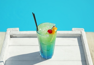 Photo of Refreshing cocktail on wooden table near swimming pool outdoors