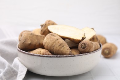 Photo of Whole and cut tubers of turnip rooted chervil in bowl on white tiled table, closeup