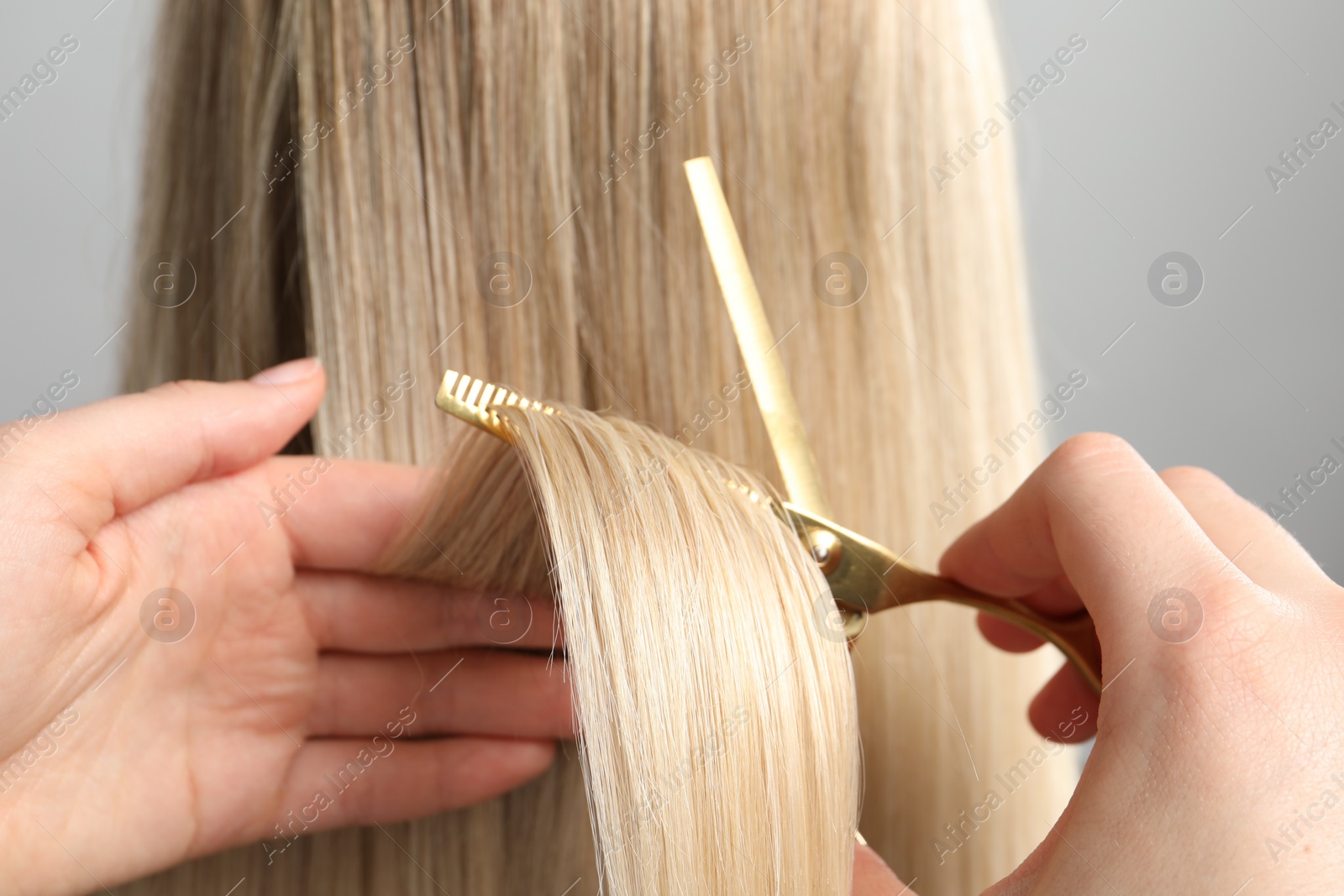 Photo of Hairdresser cutting client's hair with scissors on light grey background, closeup