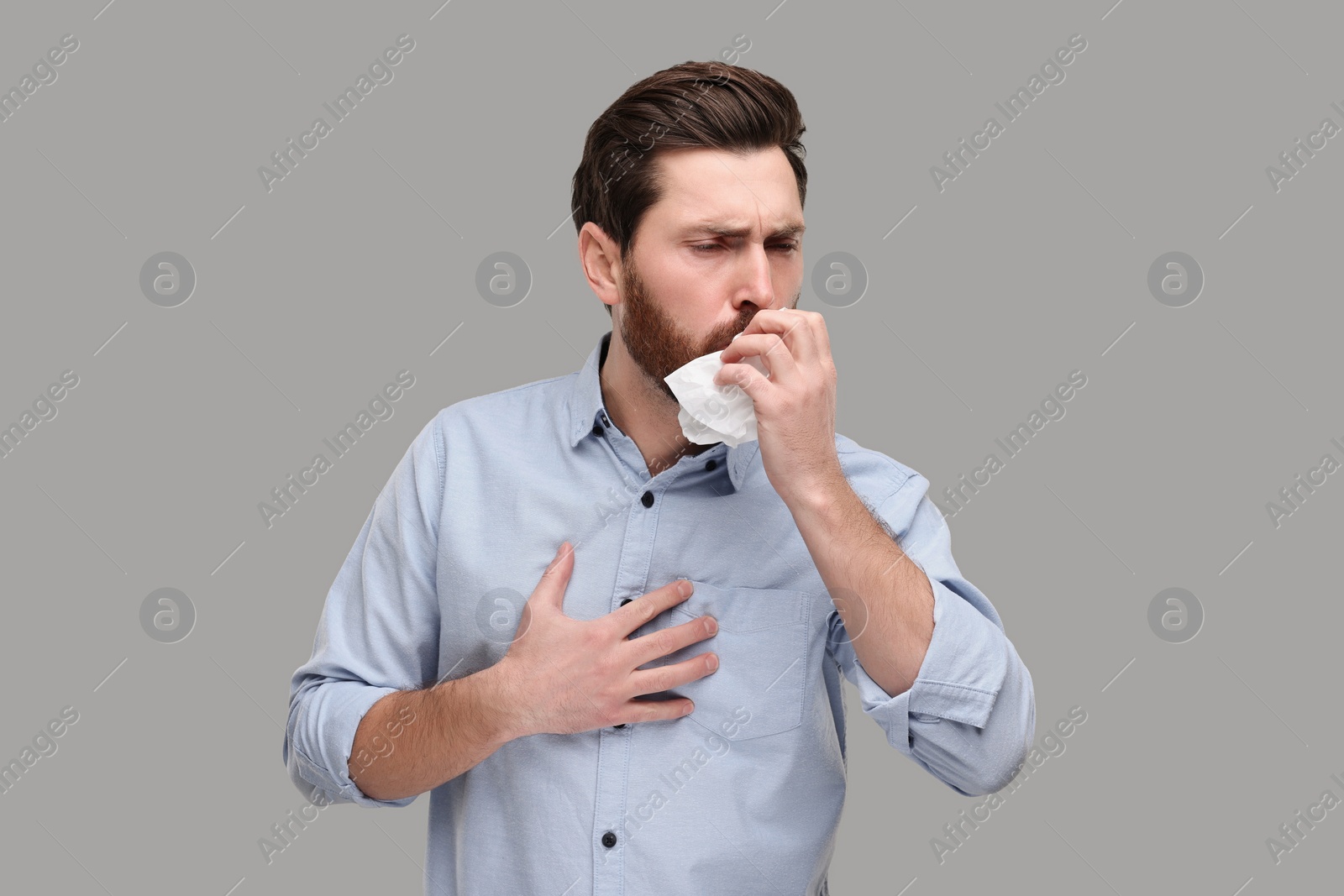 Photo of Sick man with tissue coughing on light grey background