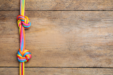 Photo of Top view of colorful ropes tied together on wooden background, space for text. Unity concept